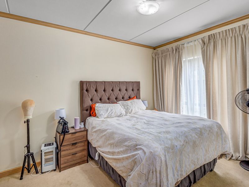 A standard bedroom featuring neutral walls, carpeted flooring, and a built-in cupboard with access to natural light through large window curtains.