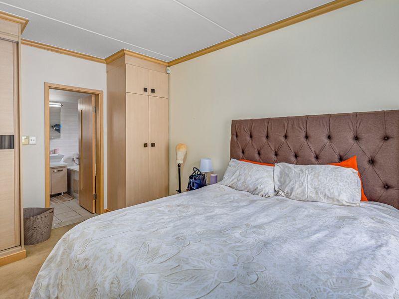 A well-lit bedroom featuring built-in wooden cupboards and direct access to an en-suite bathroom, offering a functional and comfortable living space.
