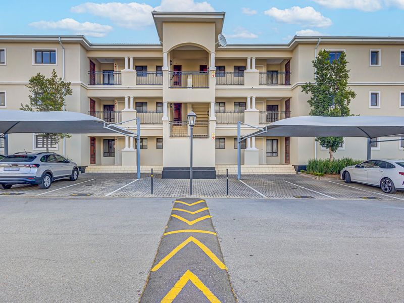 Front elevation of a multi-story apartment complex featuring paved parking bays with shade cloth carports and private balconies for each unit.
