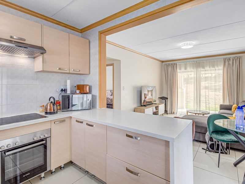 Open-plan kitchen and living area featuring light wood cabinetry, integrated appliances, tiled flooring, and direct access to an outdoor space through sliding glass doors.