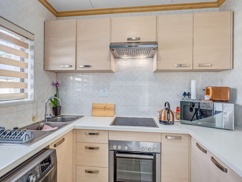 A functional kitchen featuring light wood-tone cabinetry, integrated appliances including an oven and hob, and a clean tiled backsplash.