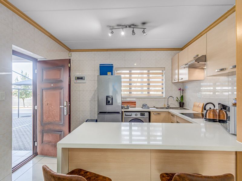 A functional kitchen featuring light wood cabinetry, stone countertops, a tiled backsplash, and integrated appliances, with direct access to an outdoor area.