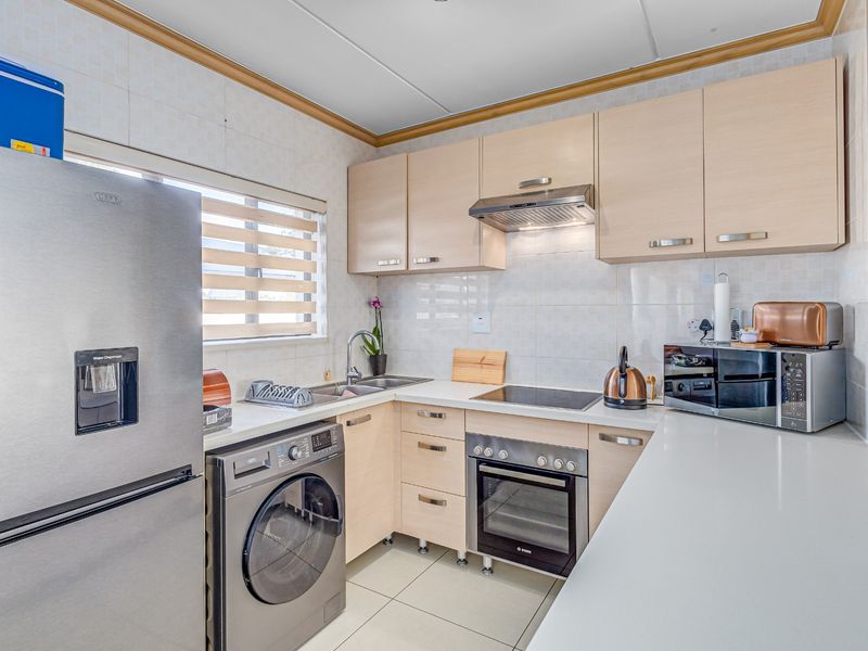 Compact kitchen featuring light wood cabinetry, integrated oven and hob, stainless steel sink, and tiled finishes, offering a functional and well-maintained workspace.