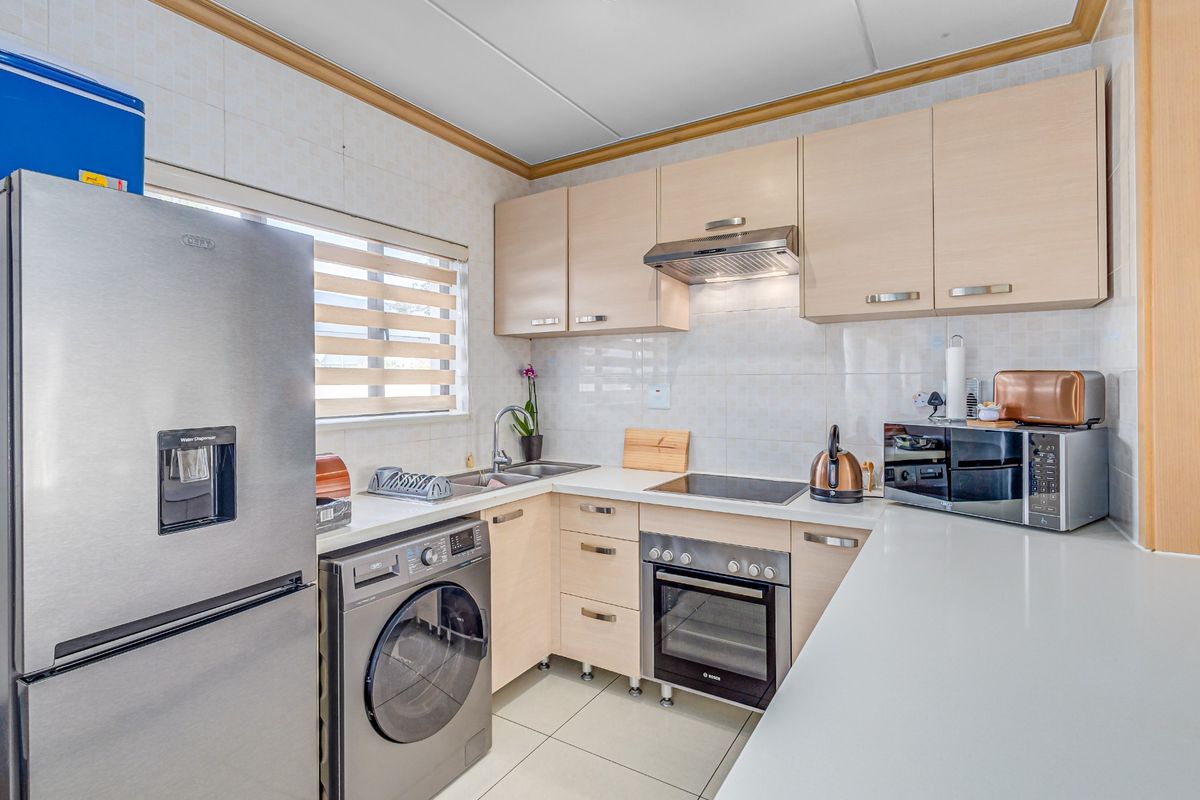 Compact kitchen featuring light wood cabinetry, integrated oven and hob, stainless steel sink, and tiled finishes, offering a functional and well-maintained workspace.