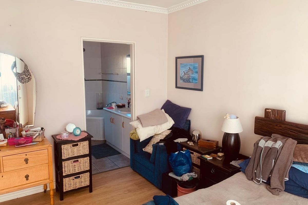 A bedroom featuring laminate flooring and crown molding, with direct access to an en-suite bathroom.