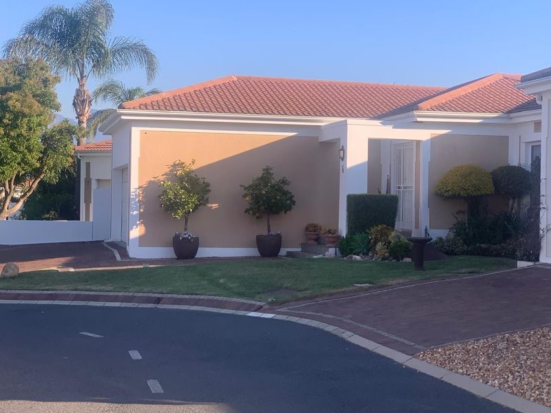 Front elevation of a residential house featuring a tiled roof, paved driveway, and a secure entrance area with landscaped garden beds.