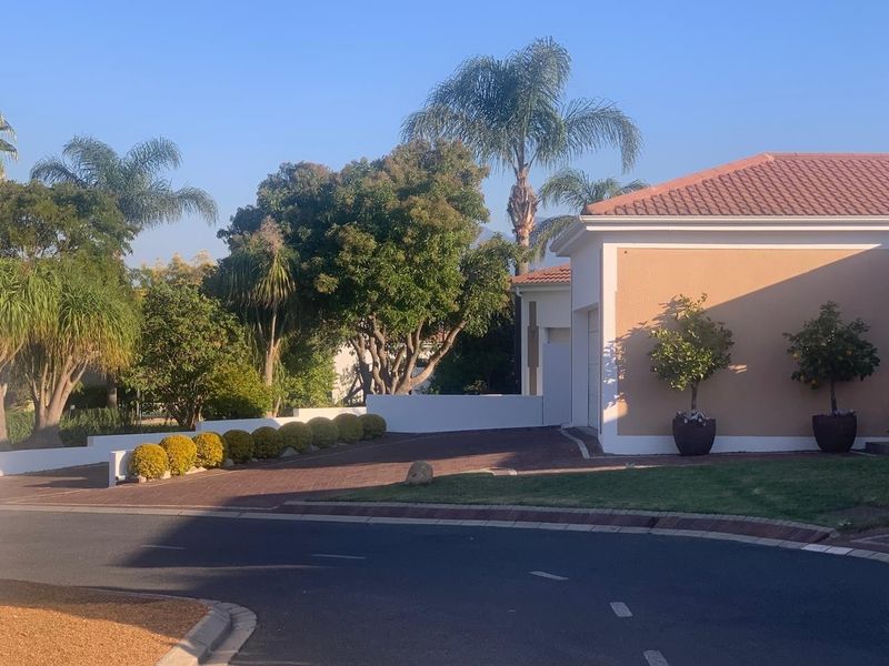 Front view of a residential property featuring a paved driveway, stucco exterior walls, and a tiled roof with established garden landscaping.