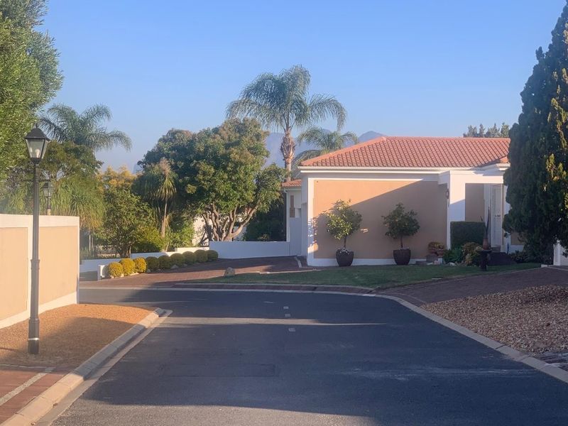 A view of the street approach showing the property's exterior facade, paved driveway, and well-maintained garden area.