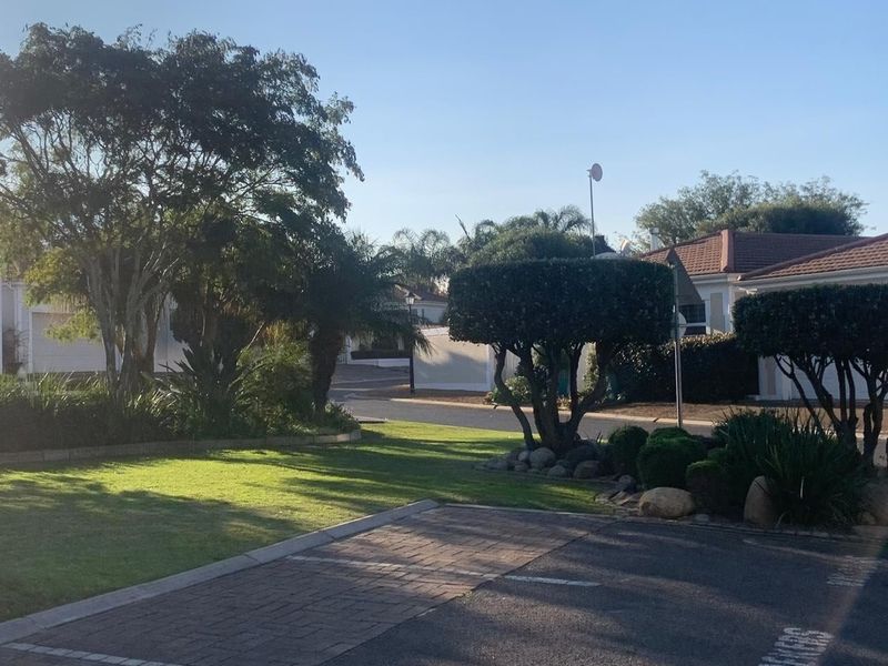 A view of a well-maintained residential street featuring paved driveways, manicured gardens, and mature trees within a quiet estate setting.