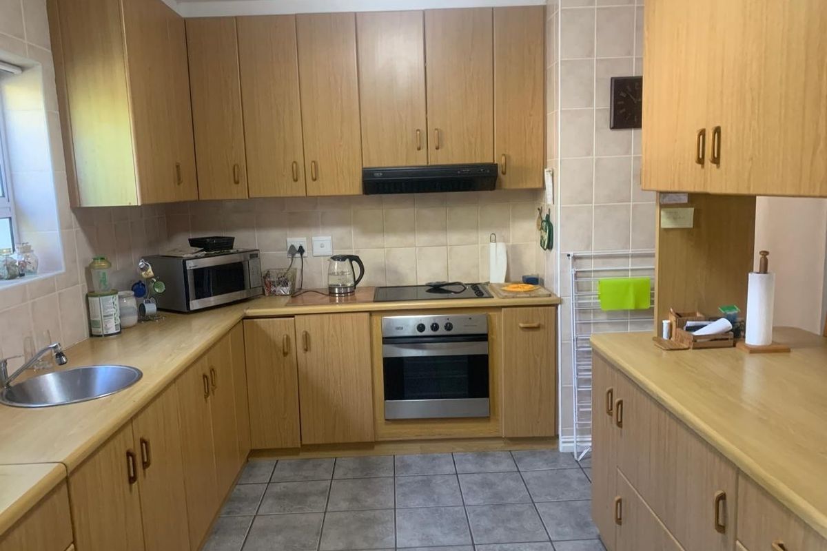 A functional kitchen featuring light wood-tone cabinetry, laminate countertops, a built-in oven with electric hob, and tiled flooring.