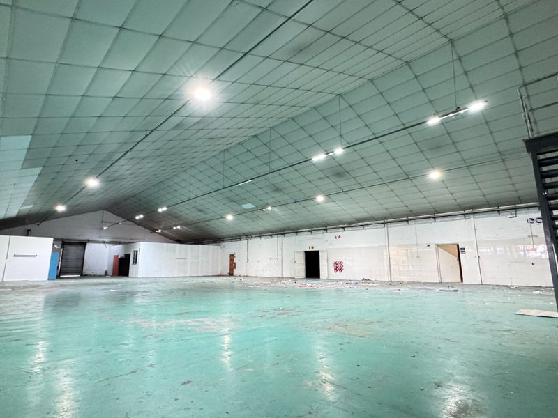 Large open-plan industrial utility space featuring a high metal ceiling, painted concrete flooring, and an integrated metal staircase.