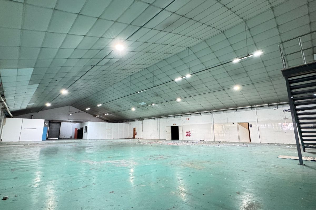 Large open-plan industrial utility space featuring a high metal ceiling, painted concrete flooring, and an integrated metal staircase.