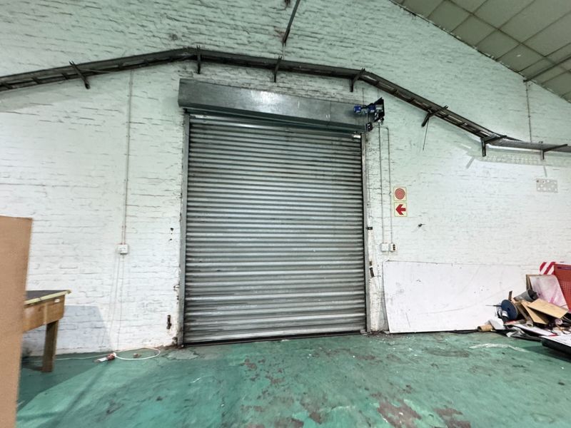 Industrial warehouse utility space featuring a large roller shutter door, exposed brick walls, and overhead cable trays.