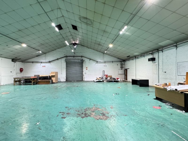 Spacious industrial warehouse unit featuring a high-clearance ceiling, roller shutter door access, and durable painted concrete flooring, suitable for various commercial or storage uses.
