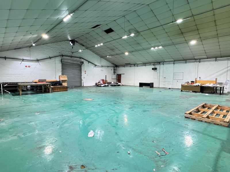 Spacious industrial warehouse unit featuring a high-clearance ceiling, roller shutter door access, and durable painted concrete flooring, suitable for various commercial or storage applications.