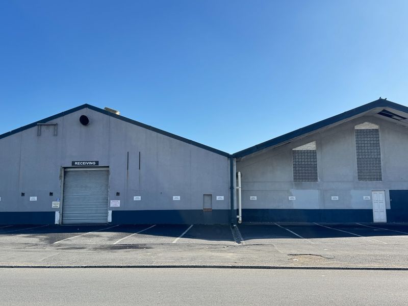 Front elevation of an industrial warehouse facility featuring a roller shutter receiving door, glass block windows, and dedicated asphalt parking bays.