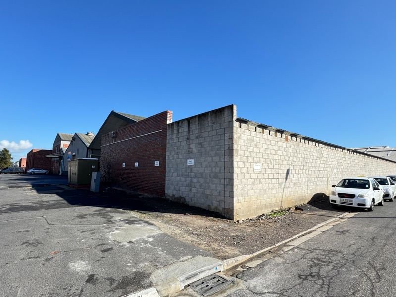 Exterior view of an industrial property featuring a large perimeter boundary wall and an expansive asphalt driveway area.