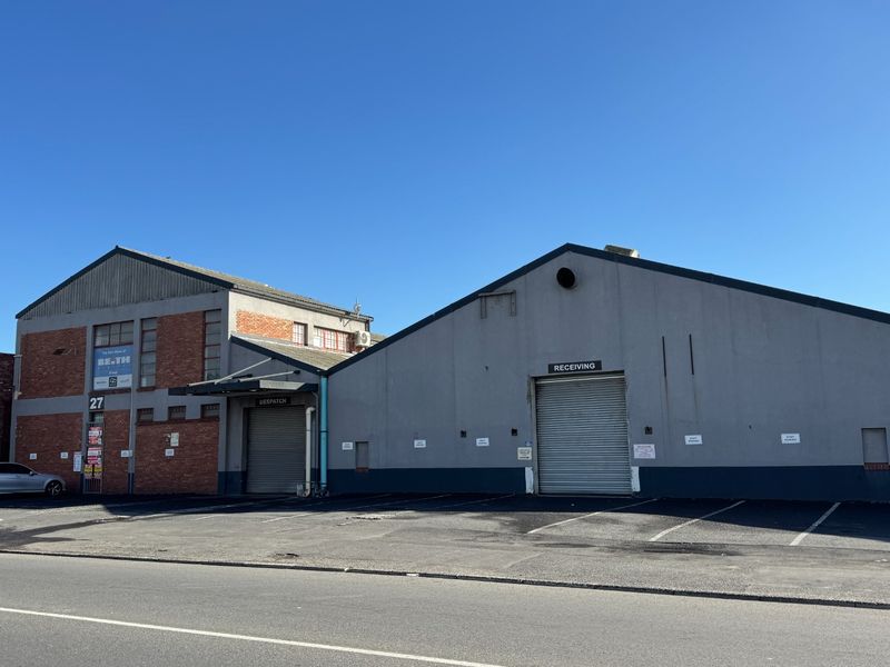 Industrial property exterior featuring multiple roller shutter doors for receiving and dispatch, with an asphalt driveway and brick and concrete facade.