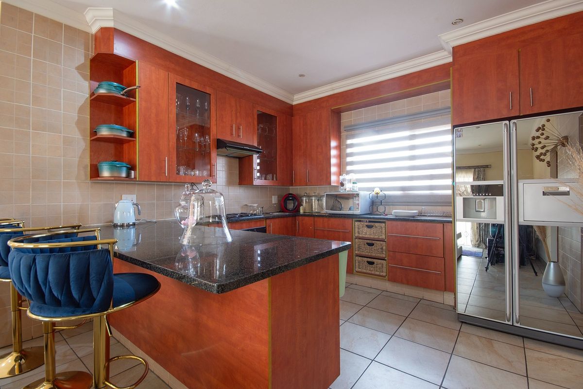 A well-maintained kitchen featuring warm-toned wooden cabinetry, granite countertops, a breakfast bar, and tiled finishes, offering a functional and classic cooking space.