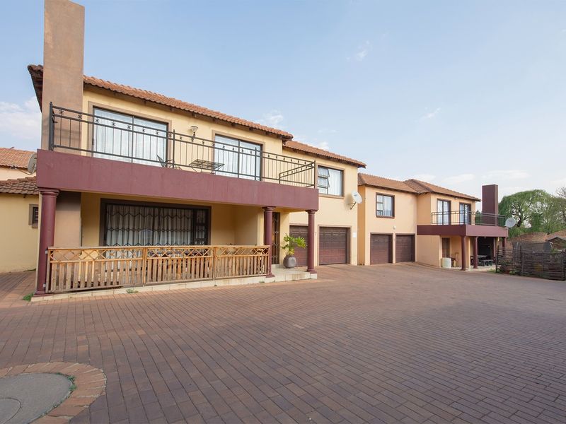 Front elevation of a townhouse complex featuring paved driveway access, multiple garage doors, and upper-level balconies with wrought iron railings.