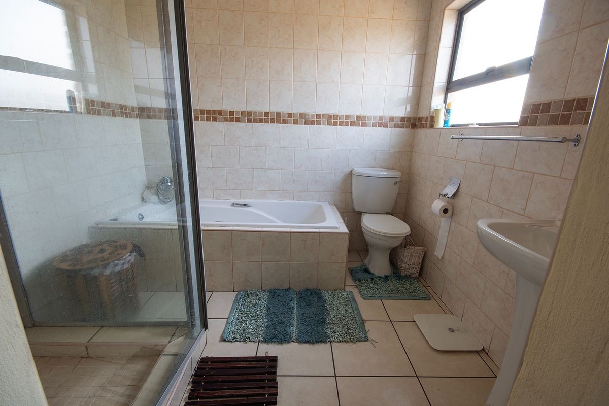 A functional bathroom featuring a built-in bathtub, separate glass shower enclosure, pedestal basin, and toilet with neutral ceramic tiling throughout.