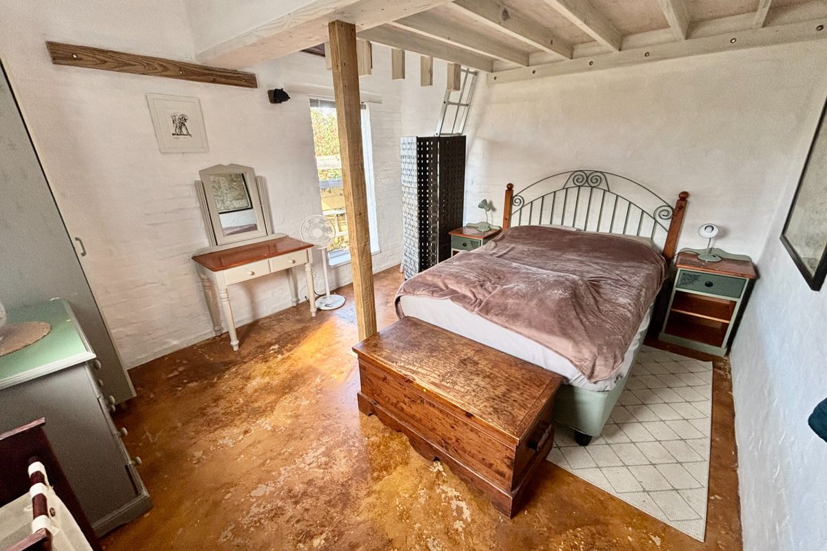 A rustic bedroom featuring exposed timber ceiling beams, a central support post, painted brick walls, and polished concrete flooring.
