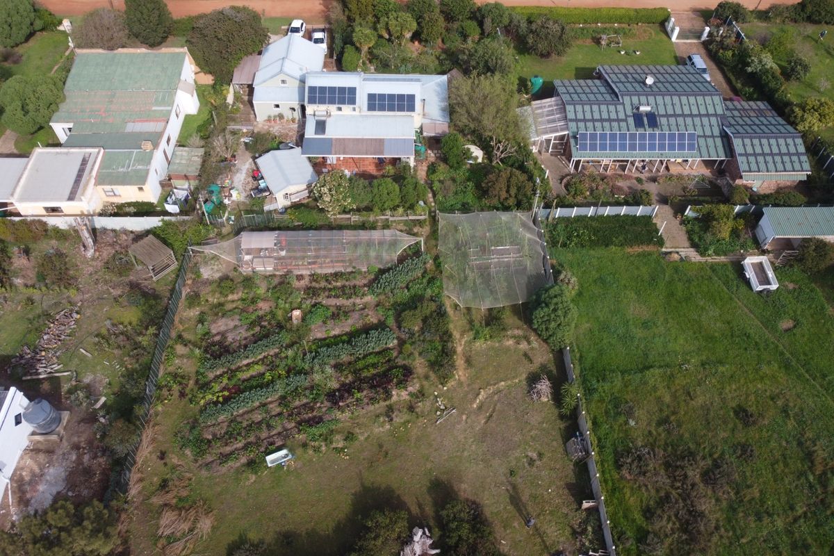Aerial view of a residential property featuring multiple buildings with solar panel installations, extensive garden plots, and established landscaping.