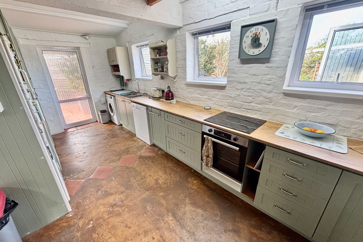 A rustic-style kitchen featuring painted brick walls, exposed timber beams, wooden countertops, and integrated appliances with a unique concrete floor finish.