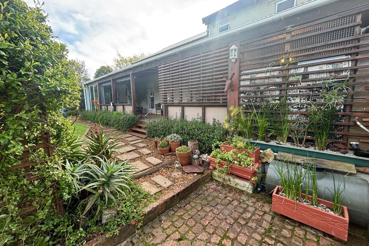 Rear exterior view featuring a covered patio, timber privacy screening, cobblestone pathways, and established garden landscaping.