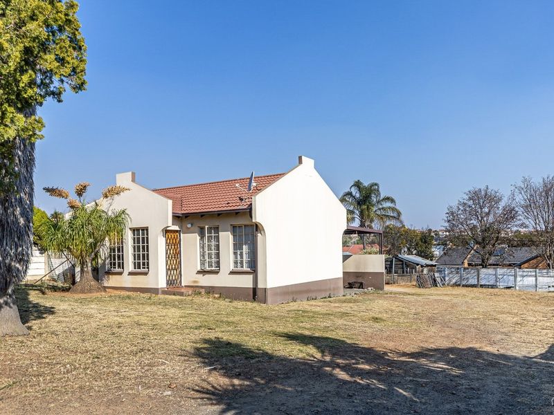 Rear view of a detached house featuring a tiled roof, security gate, and a large surrounding garden area.