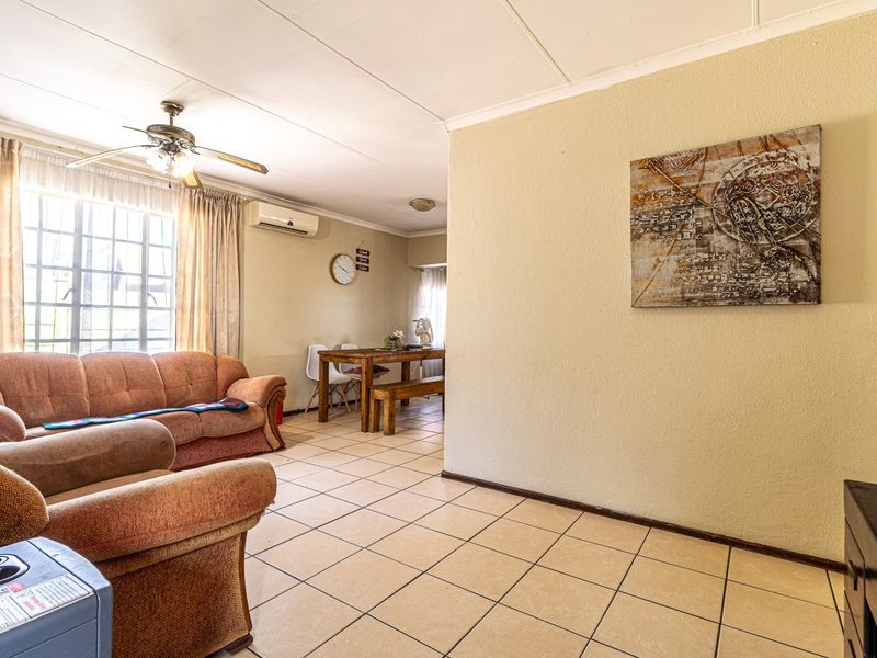 Open-plan living and dining area featuring tiled flooring, a ceiling fan, and a wall-mounted air conditioning unit.
