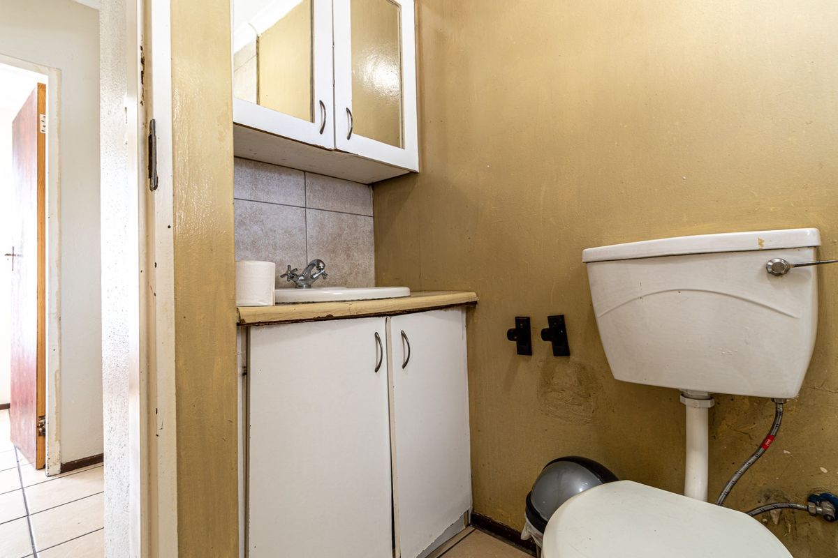 A compact bathroom featuring a basic vanity unit with basin, wall-mounted medicine cabinet, and a standard toilet, requiring cosmetic updates and maintenance.