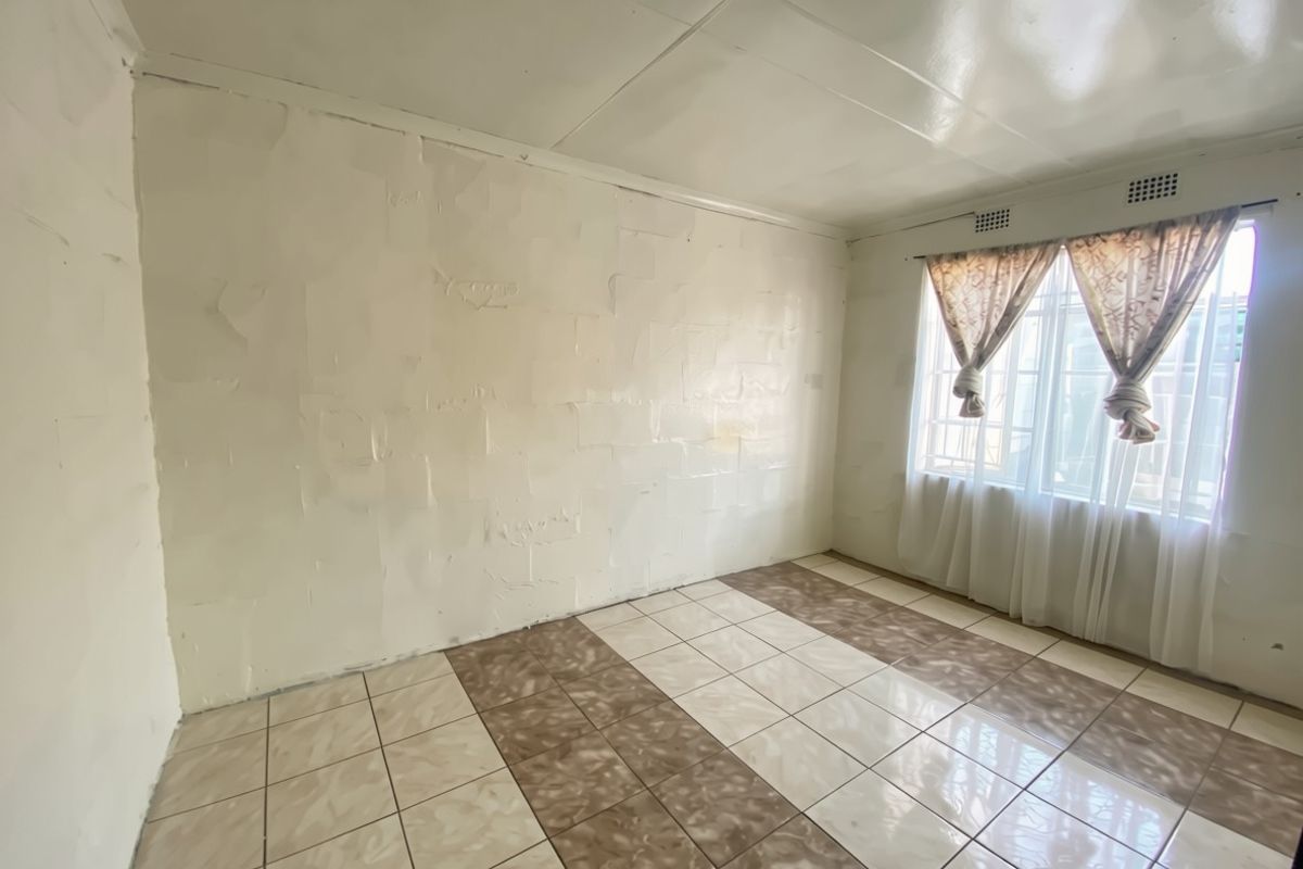 An empty bedroom featuring tiled flooring, a window with security bars, and walls requiring cosmetic attention and finishing.