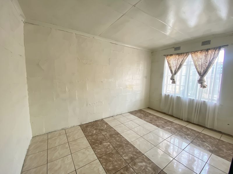 An empty bedroom featuring tiled flooring, a window with security bars, and walls requiring cosmetic attention and finishing.