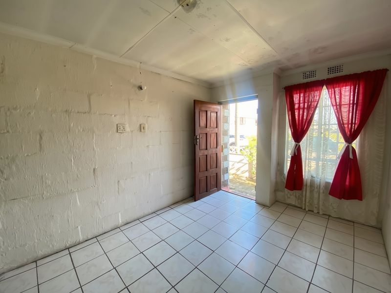 An empty living area featuring tiled flooring, exposed brick walls, and direct access to the exterior through a timber door.