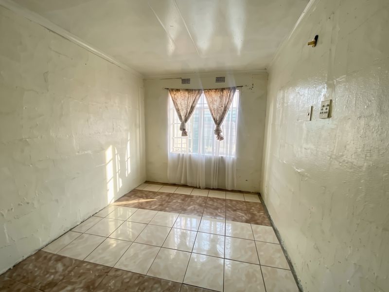 An empty bedroom featuring tiled flooring, security bars on the window, and textured wall finishes requiring cosmetic attention.