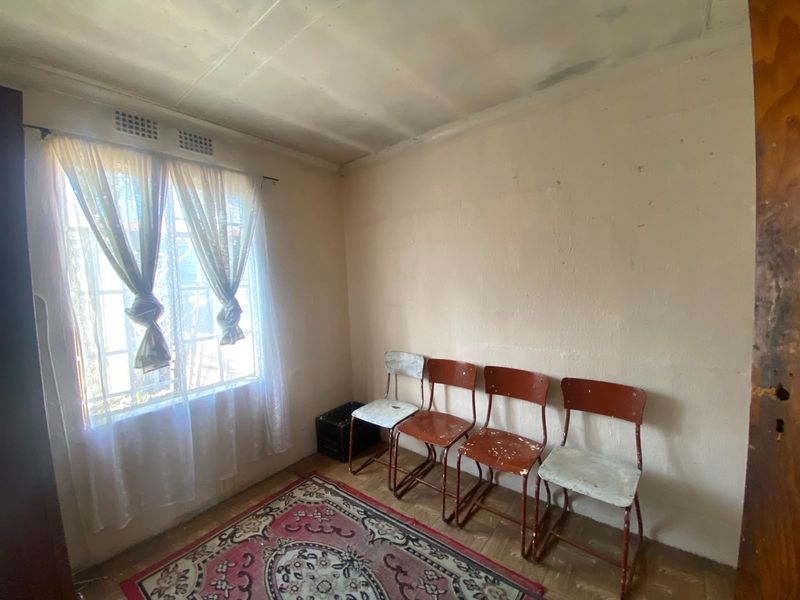 A bedroom featuring original parquet flooring and a window with security bars, requiring cosmetic updates to the walls and ceiling.