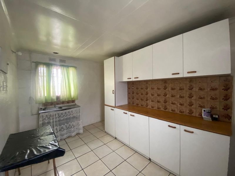 A functional kitchen featuring white built-in cabinetry, a laminate countertop, double stainless steel sink, and ceramic tile flooring.