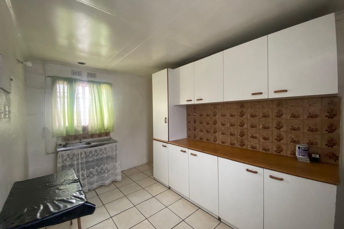A functional kitchen featuring white built-in cabinetry, a laminate countertop, double stainless steel sink, and ceramic tile flooring.