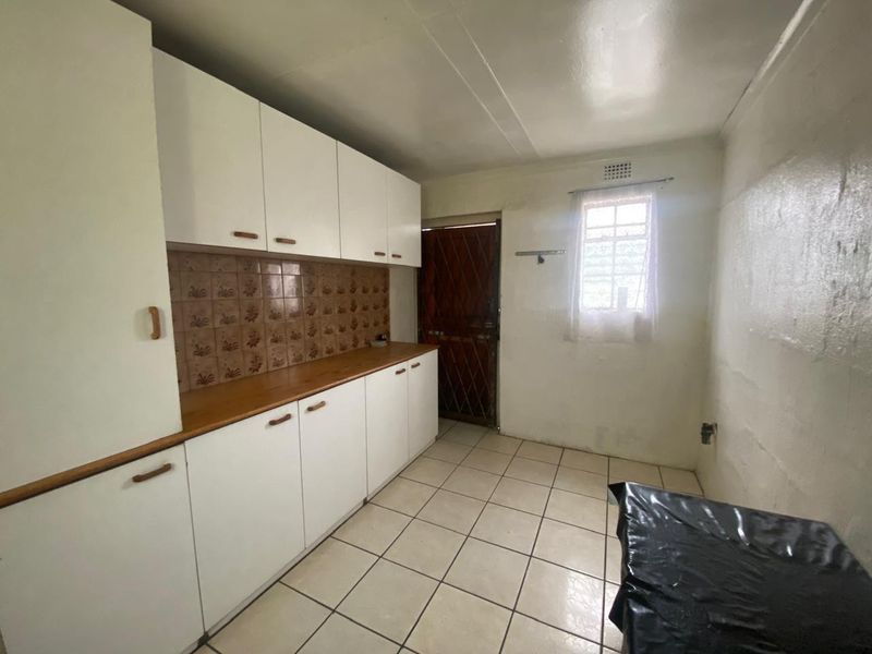 A functional kitchen space featuring white built-in cabinetry, tiled flooring, and a tiled backsplash, providing a clean canvas for potential modern updates.