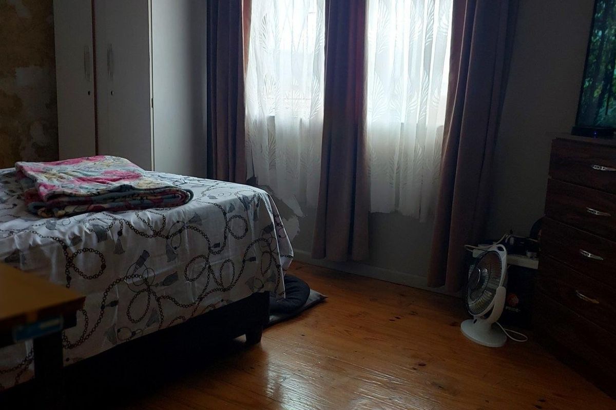 A bedroom featuring timber flooring and built-in wardrobe storage, currently showing signs of wear including peeling wallpaper.