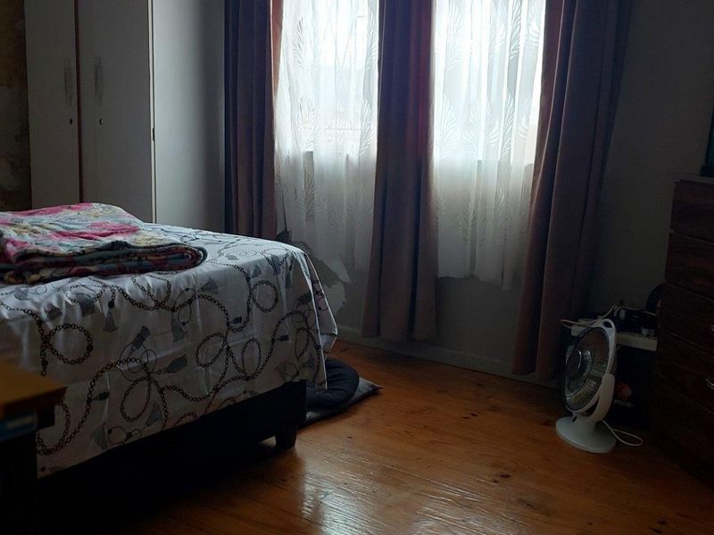A bedroom featuring timber flooring and built-in wardrobe storage, currently showing signs of wear including peeling wallpaper.
