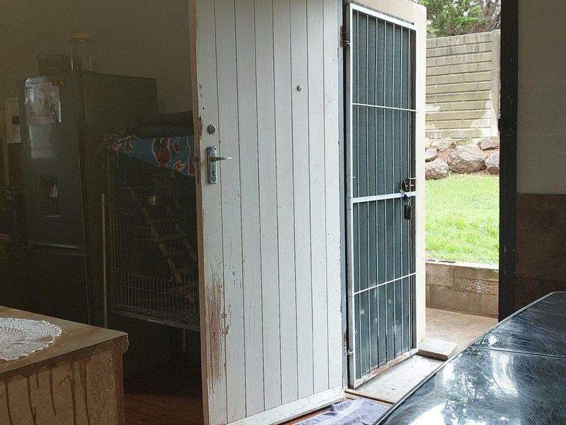 A functional kitchen area featuring a stainless steel sink, tiled splashback, and direct access to the rear garden through a security gate.
