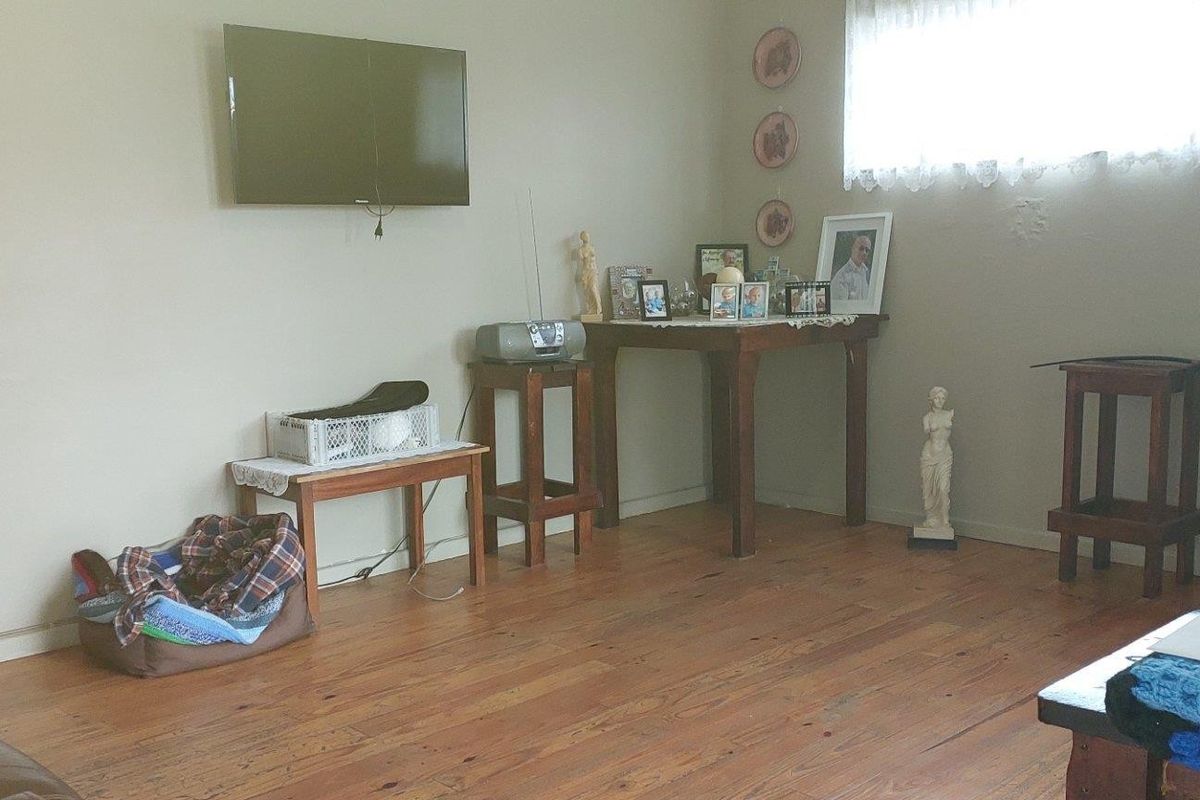 A living room featuring hardwood flooring and a wall-mounted television, offering a functional space with potential for modern updates.