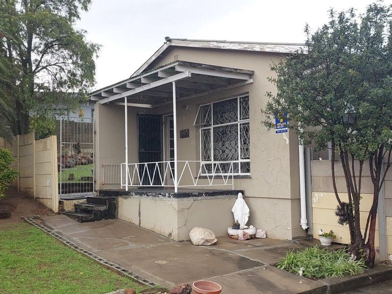 Front elevation of a single-story house featuring a covered porch, security bars, and a concrete driveway with surrounding garden area.