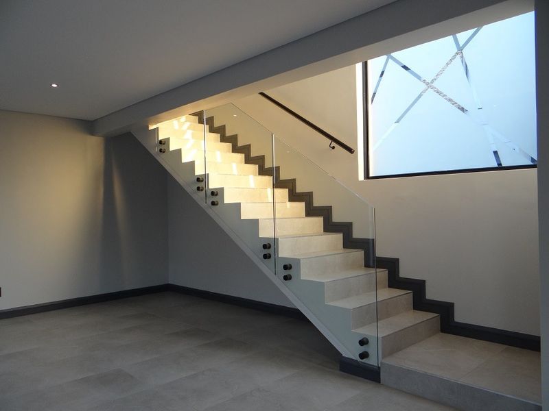 Modern hallway featuring a contemporary staircase with glass balustrades, integrated stair lighting, and large feature window, finished with high-quality floor tiling.