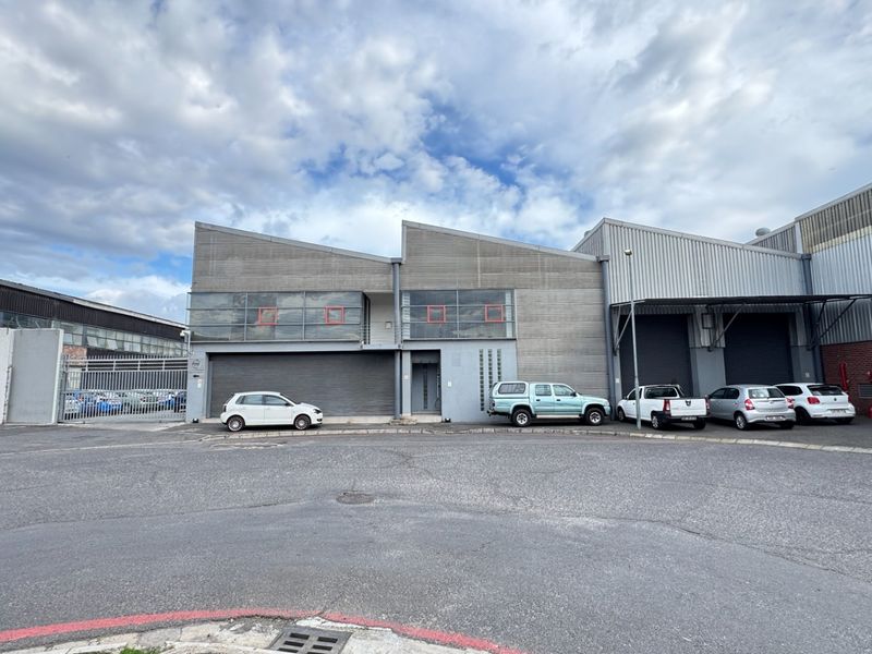 Front elevation of an industrial warehouse facility featuring metal cladding, multiple roller shutter doors, and a paved yard area.