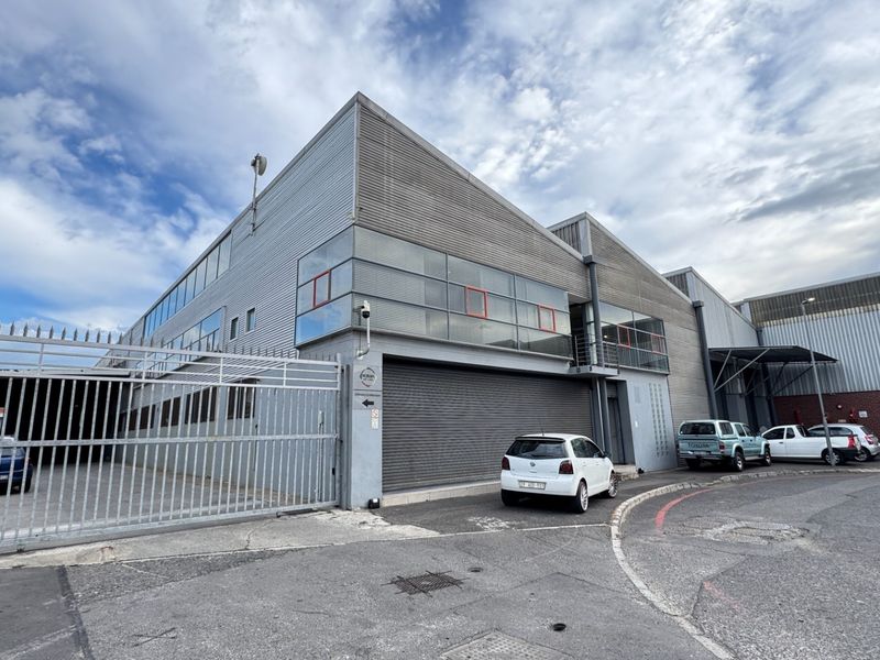Industrial facility exterior featuring corrugated metal cladding, a secure gated entrance, and a large roller shutter door for logistics access.