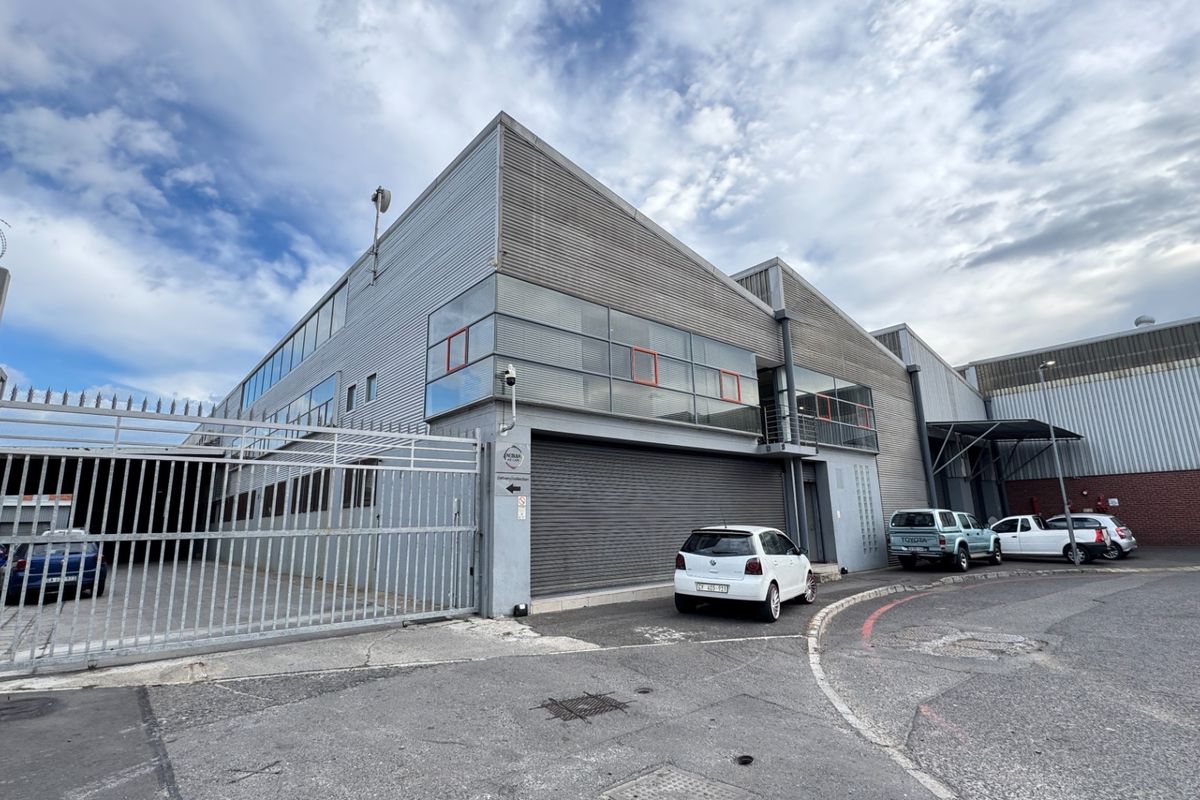 Industrial facility exterior featuring corrugated metal cladding, a secure gated entrance, and a large roller shutter door for logistics access.