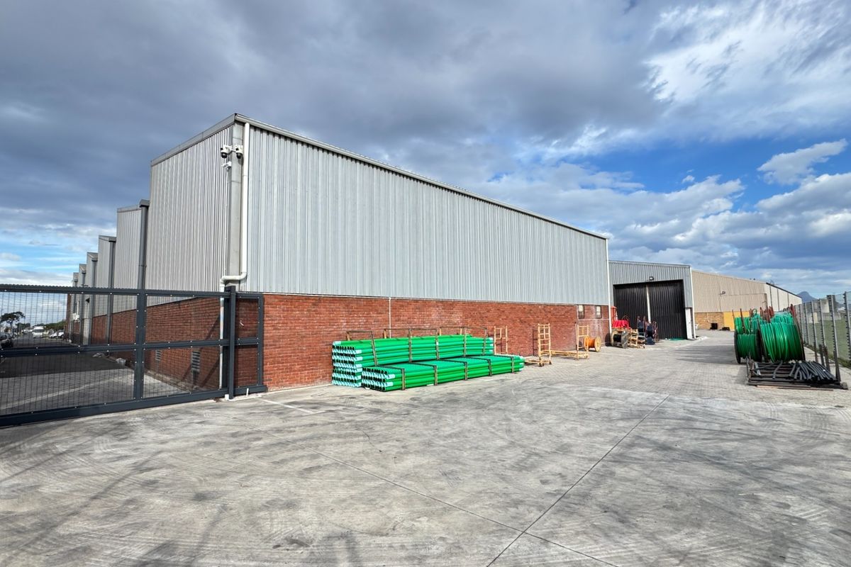 Rear exterior view of an industrial warehouse facility featuring corrugated metal cladding, face brick base, secure perimeter fencing, and a paved concrete yard.